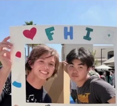 Students posing behind FHI's hand-decorated photo frame at a school fair