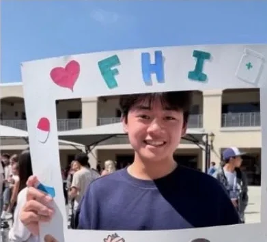 Students posing behind FHI's hand-decorated photo frame at a school fair