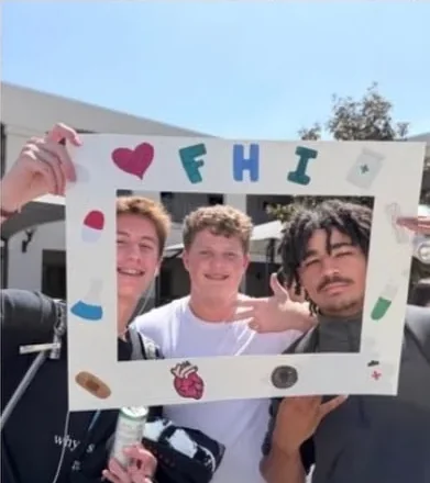 Students posing behind FHI's hand-decorated photo frame at a school fair